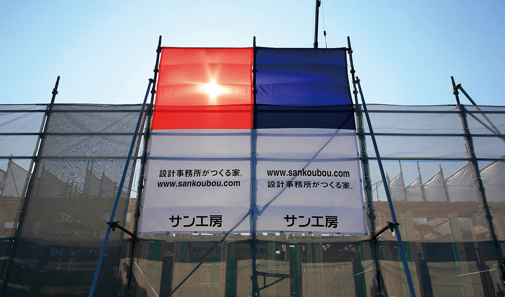 建築現場の足場に掲げられたサン工房の養生シート